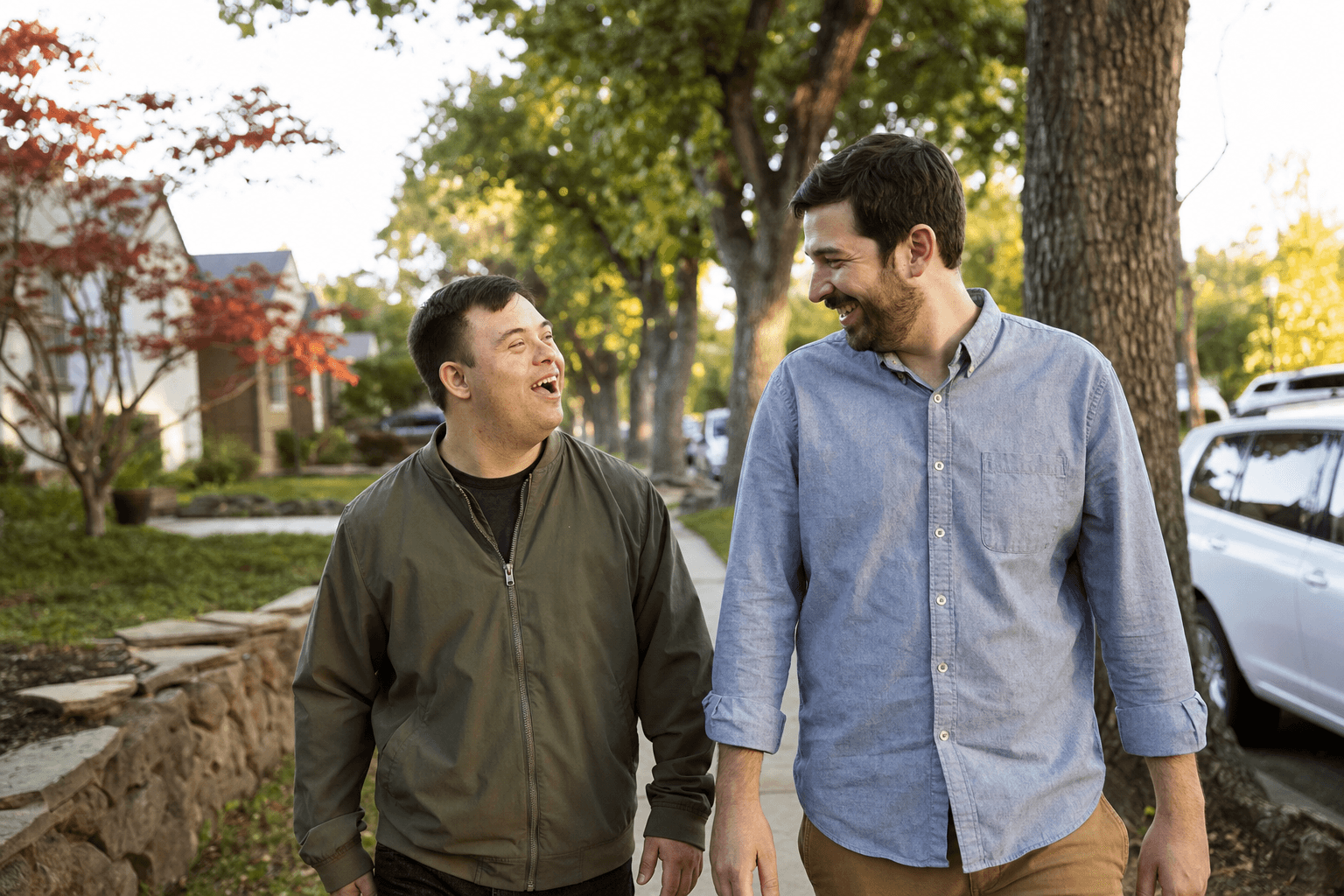 Two men walking and laughing together on a tree-lined neighborhood sidewalk.